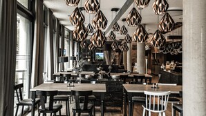 Un interior de restaurante moderno con varias mesas y sillas para comer, lámparas colgantes geométricas y una zona de bar.