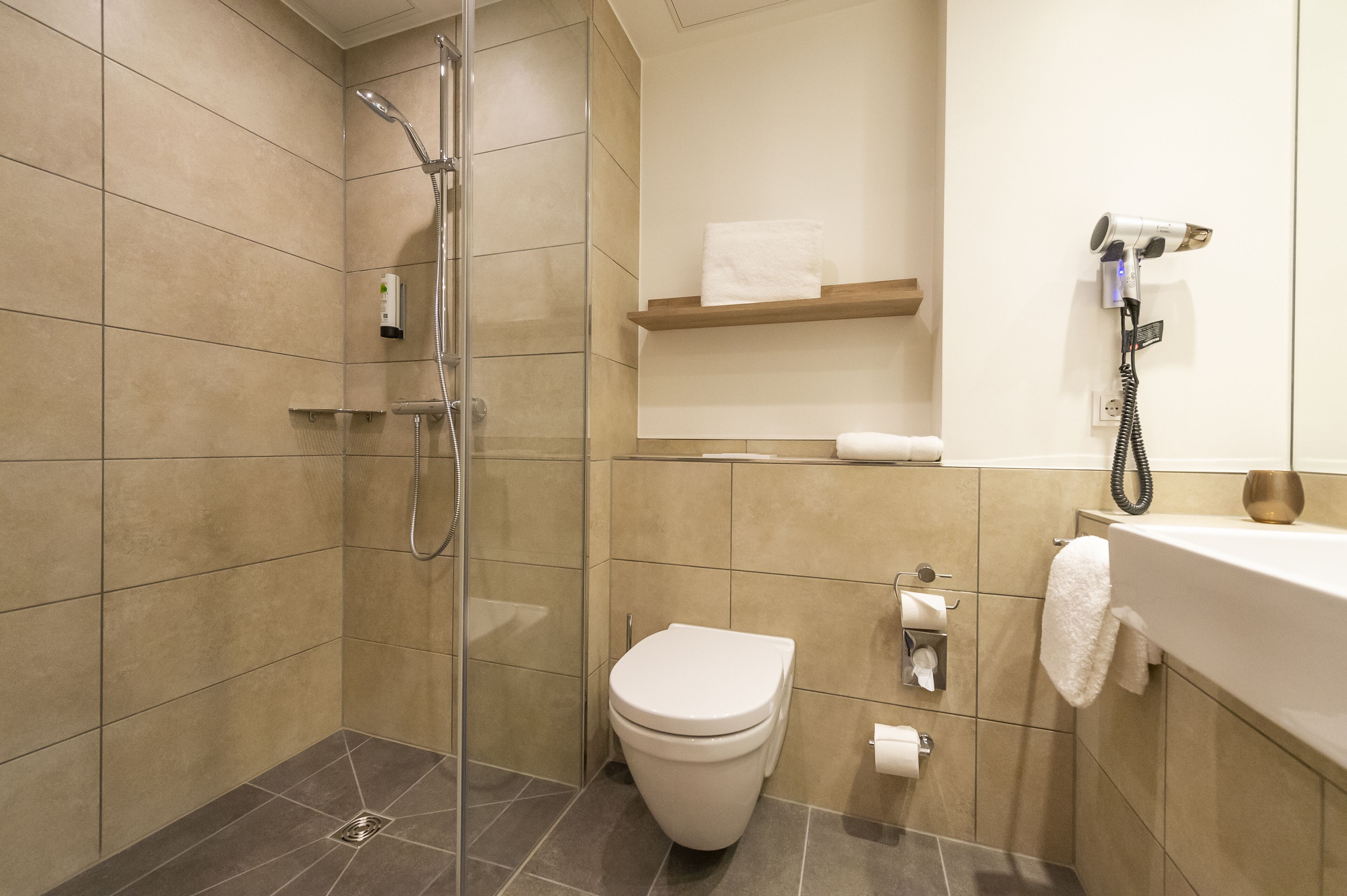 Un baño moderno con ducha de vidrio, inodoro y lavamanos con un perchero para toallas.