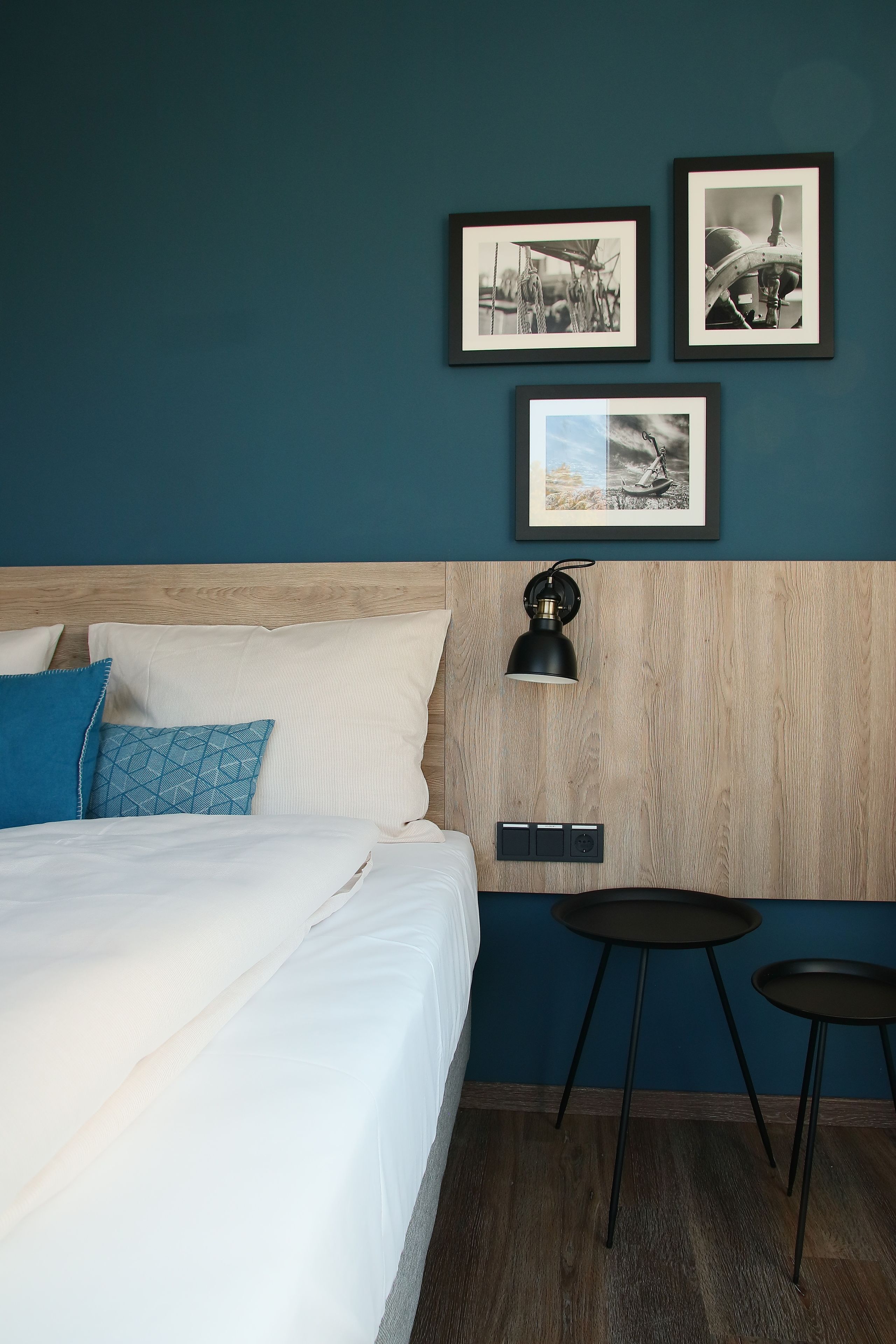 Habitación de hotel con cama, mesita de noche, lámpara y tres cuadros en la pared.