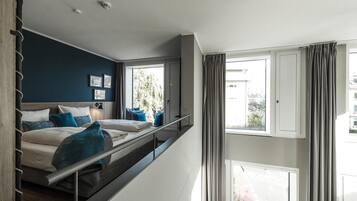 Una habitación de hotel moderna con balcón, cama con ropa de cama azul y blanca, y vista a la ciudad.