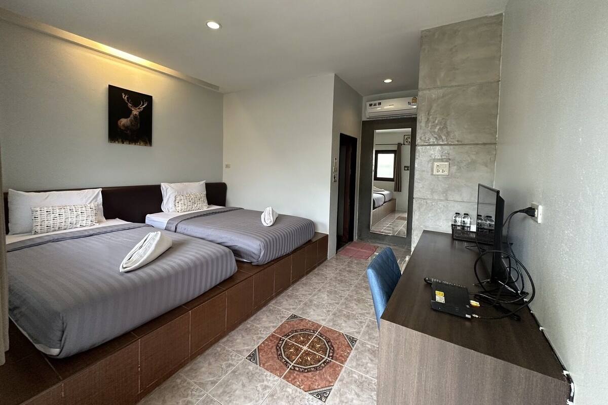 A hotel room with two beds, a desk with a computer, and a bathroom visible through an open door.