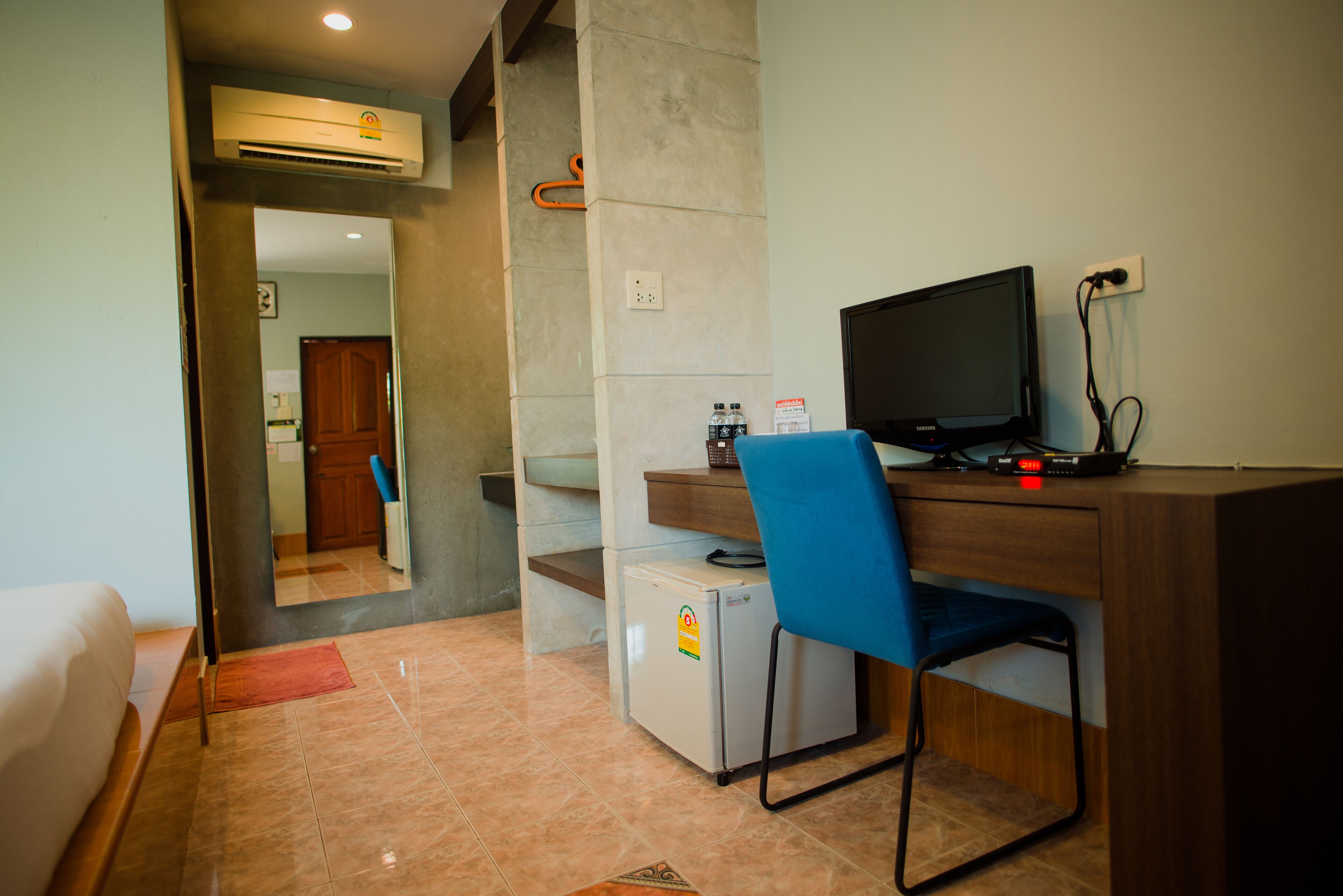 A compact hotel room with a bed, a desk with a computer, a small refrigerator, and a chair.
