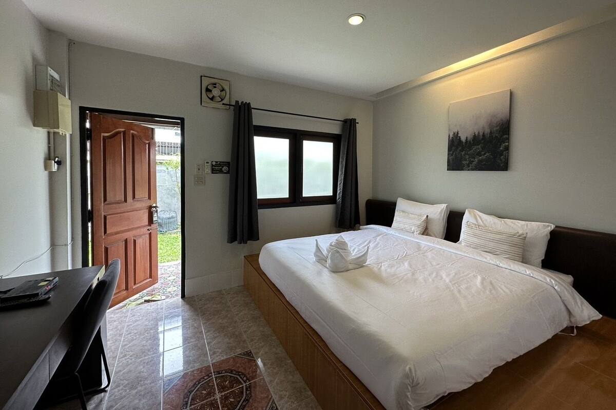 A bedroom with a bed, a desk, a window, and a door.
