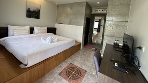 Quarto de hotel moderno com uma cama grande, uma mesa com um computador e um banheiro visível por uma porta aberta.