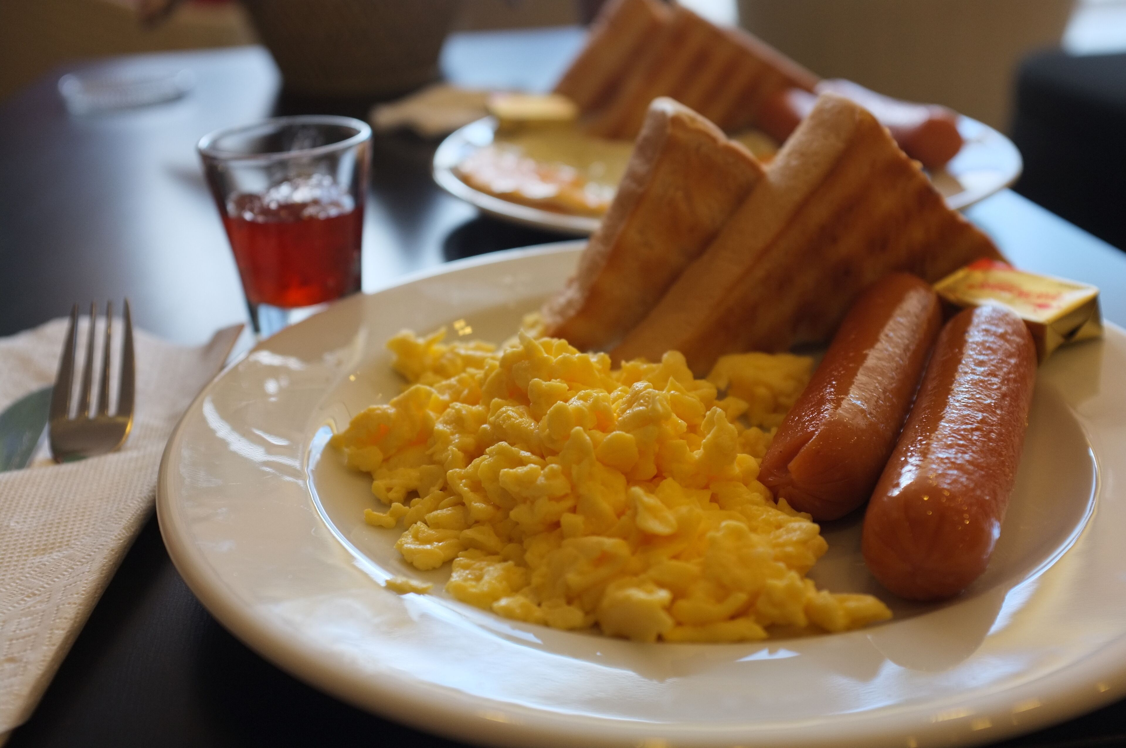 Un plat d'ous remenats, dues salsitxes i pa torrat damunt d'una taula.