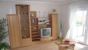 A living room with a wooden cabinet, TV, and a dining table with a vase and bottle.