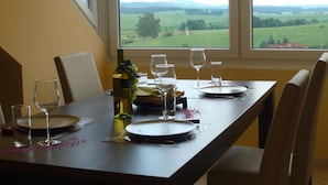 A dining table set for two with a view of a green landscape through a window.