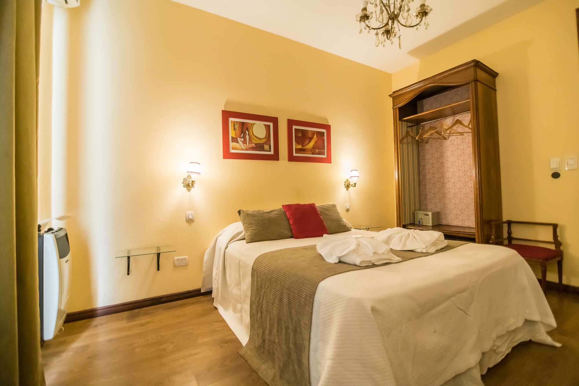 Habitación de hotel con una cama grande, dos lámparas de pared, una araña y dos cuadros enmarcados.