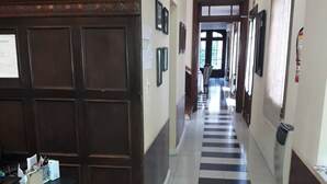 A hallway with a checkered floor, wooden doors, and a desk with papers and a computer.