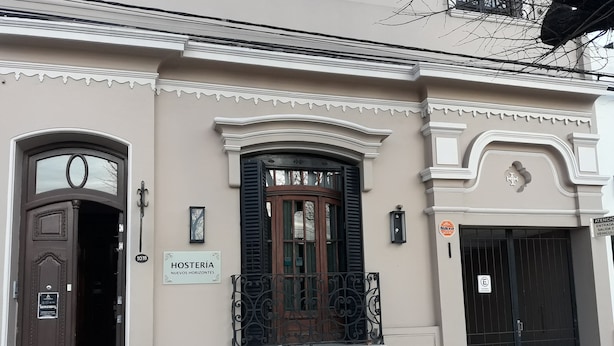 A building facade with a sign reading "HOSTERÍA NUEVOS HORIZONTES," a large arched window, and a black door with a metal gate.