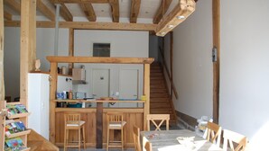 Une cuisine rustique avec des poutres en bois, un coin repas avec une table et des chaises, et un escalier menant à un autre niveau.