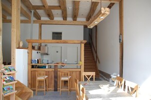 Una cocina rústica con vigas de madera, un comedor con mesa y sillas, y una escalera que sube a otro nivel.