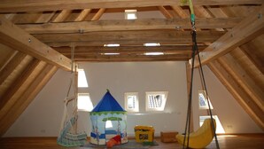 Une chambre mansardée avec un plafond en bois incliné, une tente de jeu, une balançoire suspendue et une fenêtre donnant sur l’extérieur.