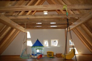 Habitación en el ático con techo de madera inclinado, una carpa de juegos, un columpio colgante y una ventana con vistas al exterior.