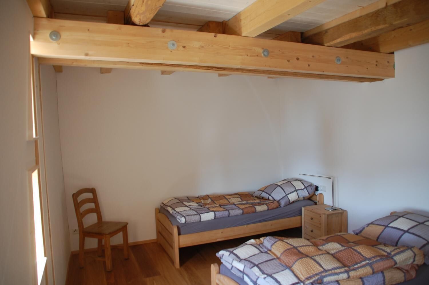 A small, single-bedroom room with a wooden bed, a chair, and a nightstand.