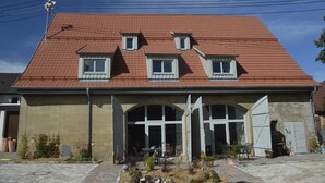 Un bâtiment à deux étages, doté d’un toit recouvert de tuiles rouges, d’une entrée centrale avec un portail en arc de cercle et d’un petit balcon à l’étage supérieur.