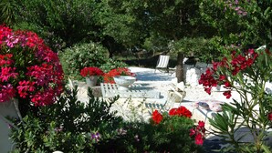 A garden patio with a white table, a white chair, and a white lounge chair. There are potted plants and flowers around the seating area. - Ulivi Al Sole - Charming B&B (Francavilla Fontana)