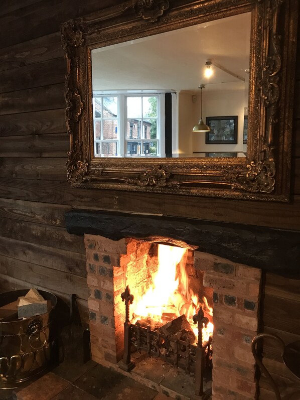 A fireplace with a mirror above it, reflecting a room with a window and a lamp. - The Kings Arms Hotel (Stafford)