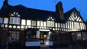 Un bâtiment de style Tudor traditionnel, avec une façade sombre, des éléments en bois peints en blanc et une entrée accueillante.