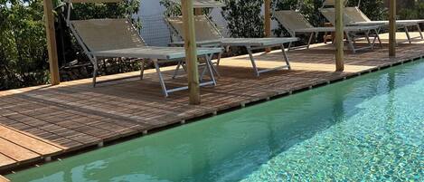 Relax by the pool surrounded by lush greenery and shaded by a pergola.