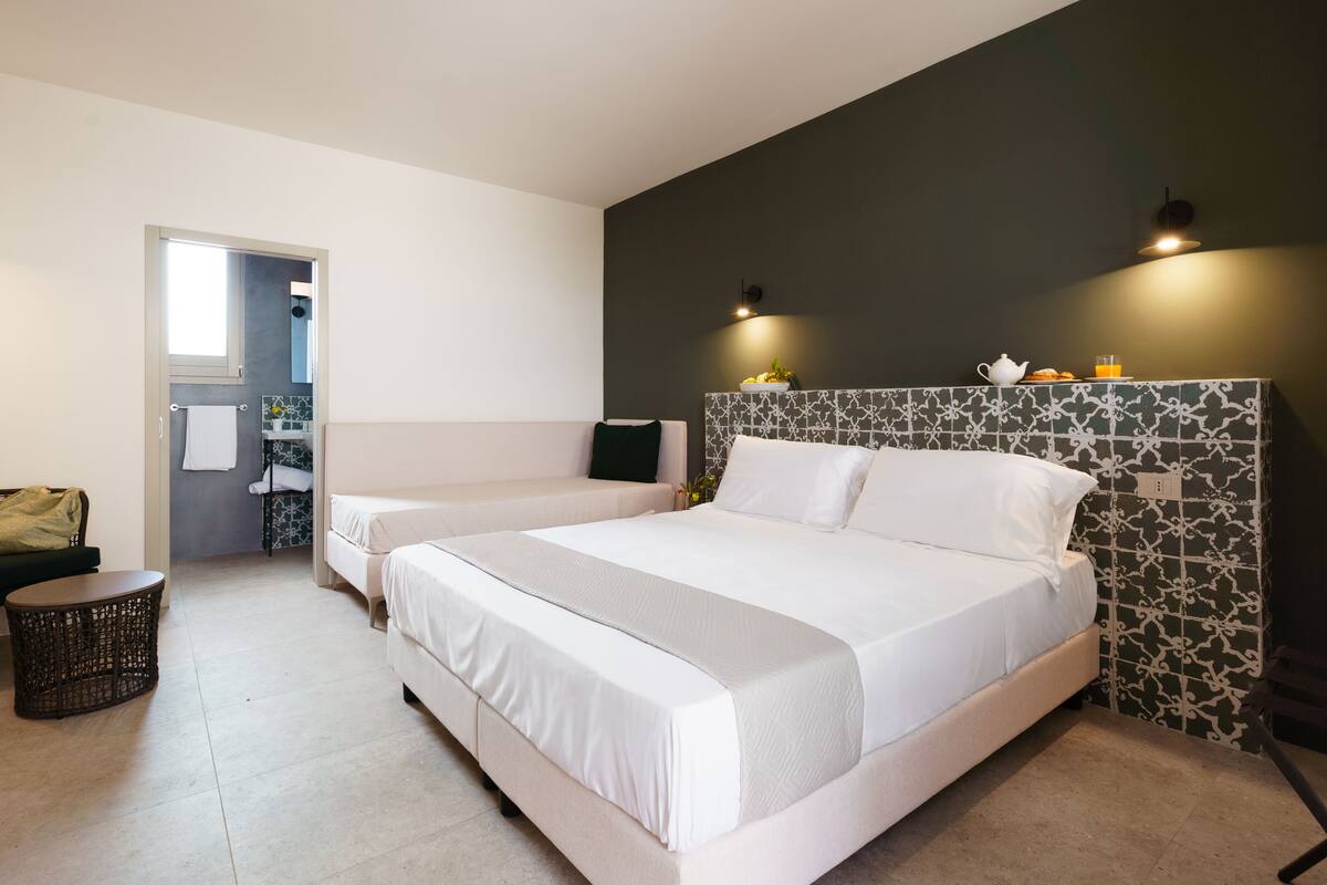 Une chambre d’hôtel moderne avec deux lits, un petit coin salon et vue sur la salle de bain.