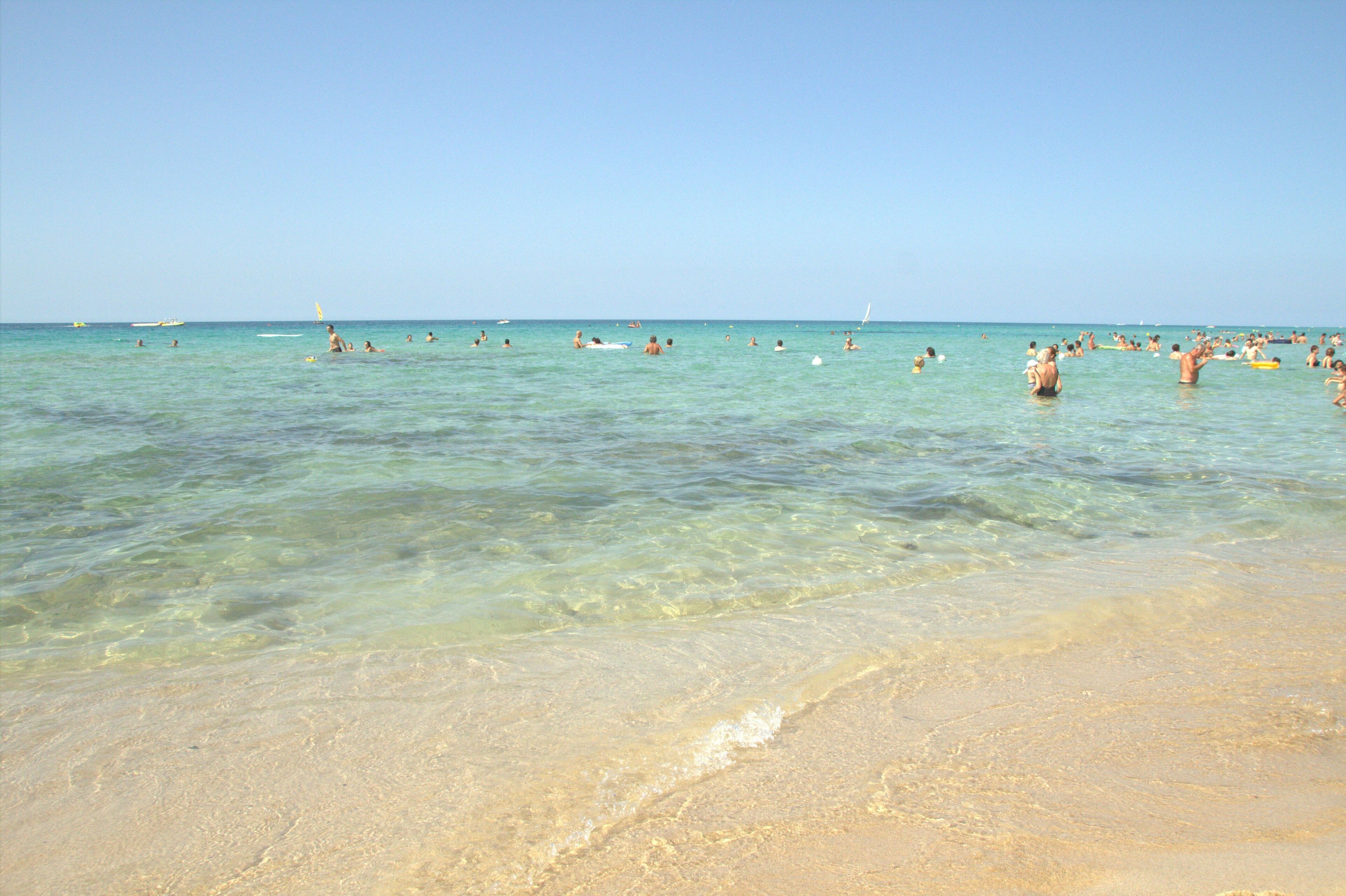 A beach with clear shallow waters and a sandy shore.
