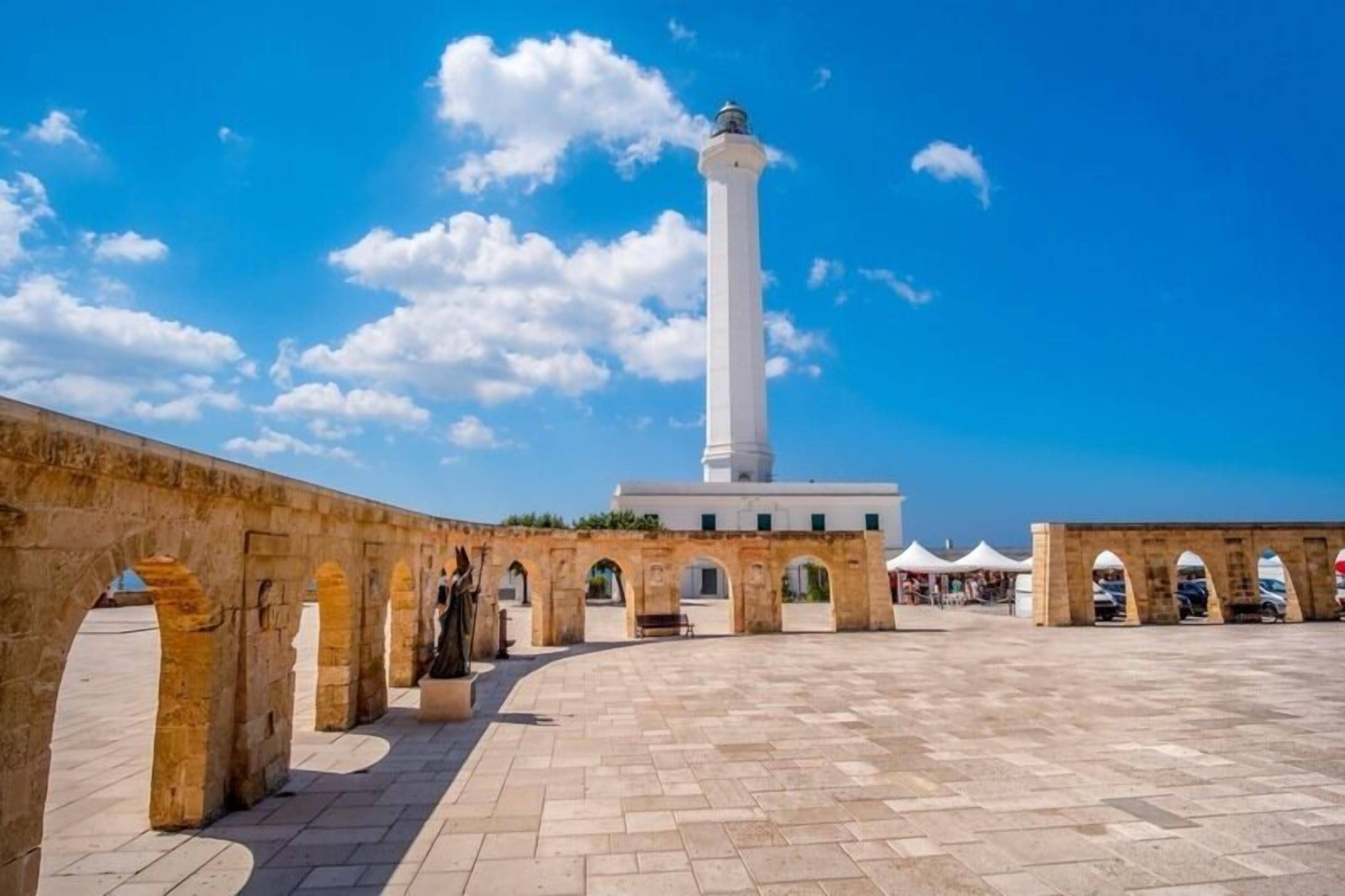 A courtyard with a tall white tower, stone arches, and a paved floor.