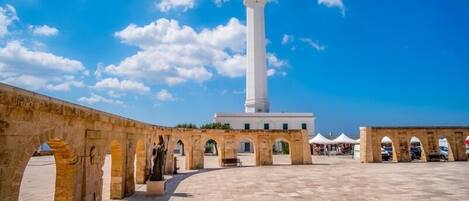 A courtyard with a tall white tower, stone arches, and a paved floor.