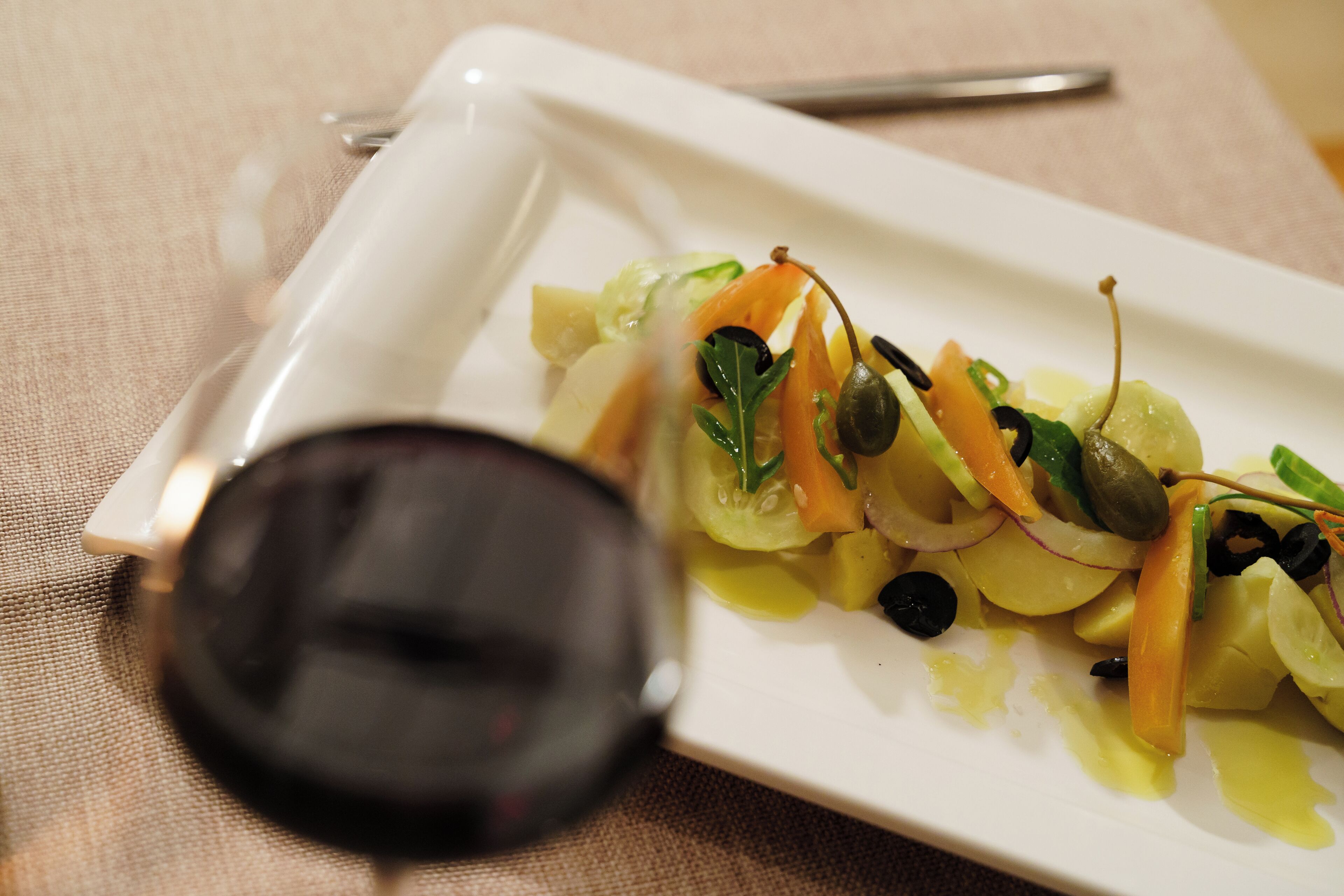 Une assiette rectangulaire blanche, sur laquelle on voit une salade, une cuillère et un verre à vin, le tout posé sur une nappe beige.