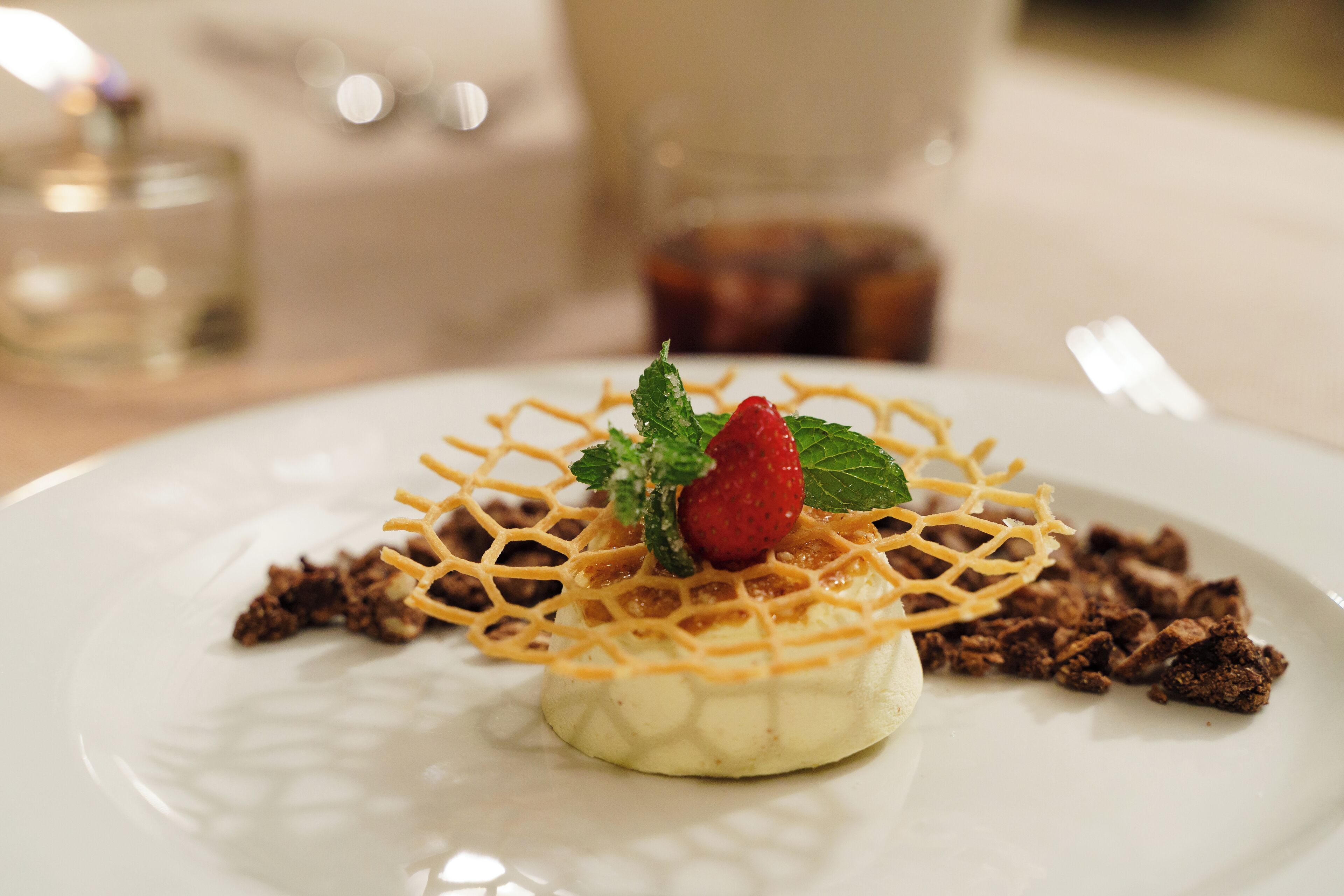 Un postre en un plato blanco con un enrejado, una fresa y hojas de menta.