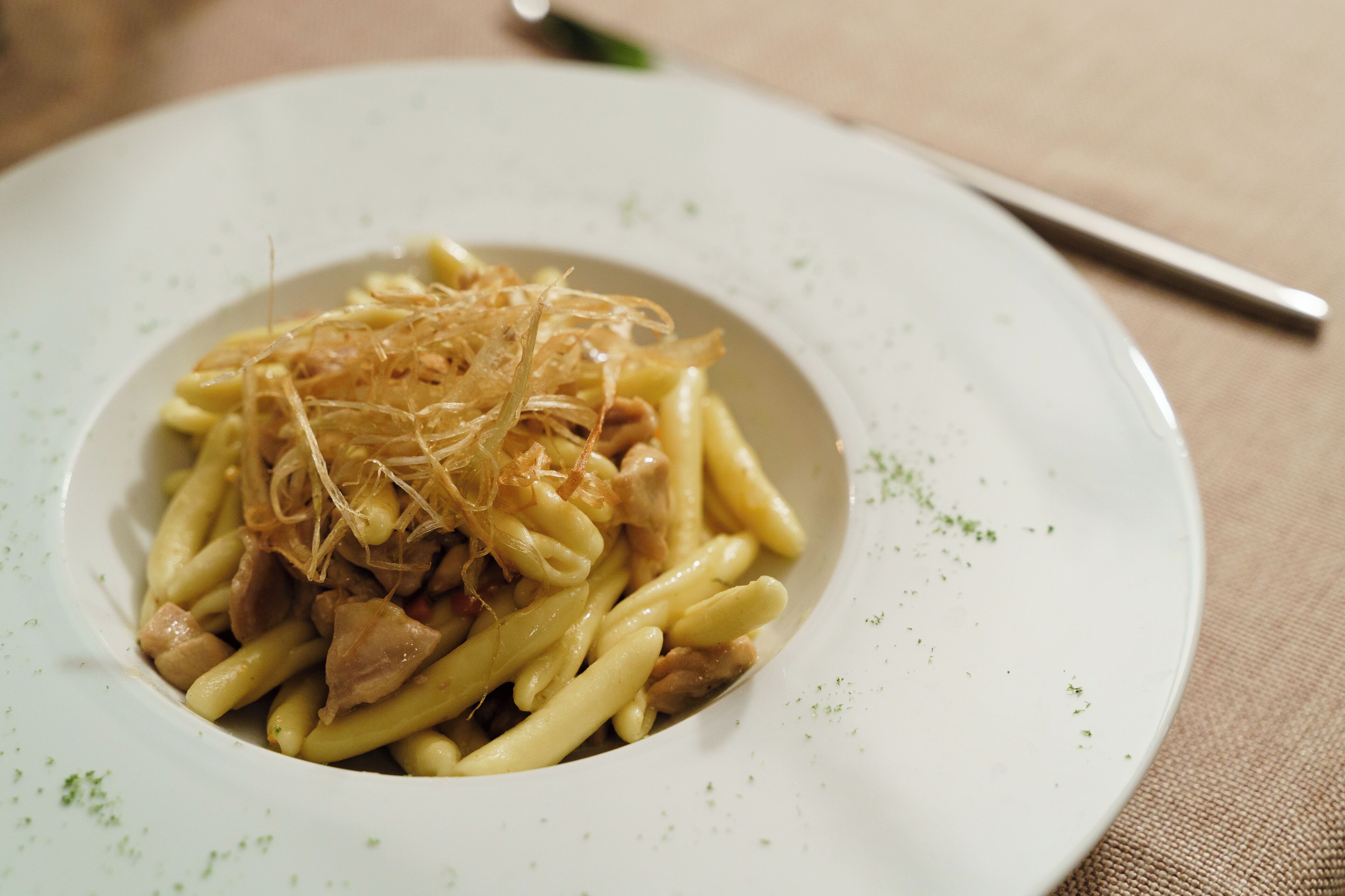 Une assiette de pâtes avec de la viande, garnie de lamelles croustillantes.