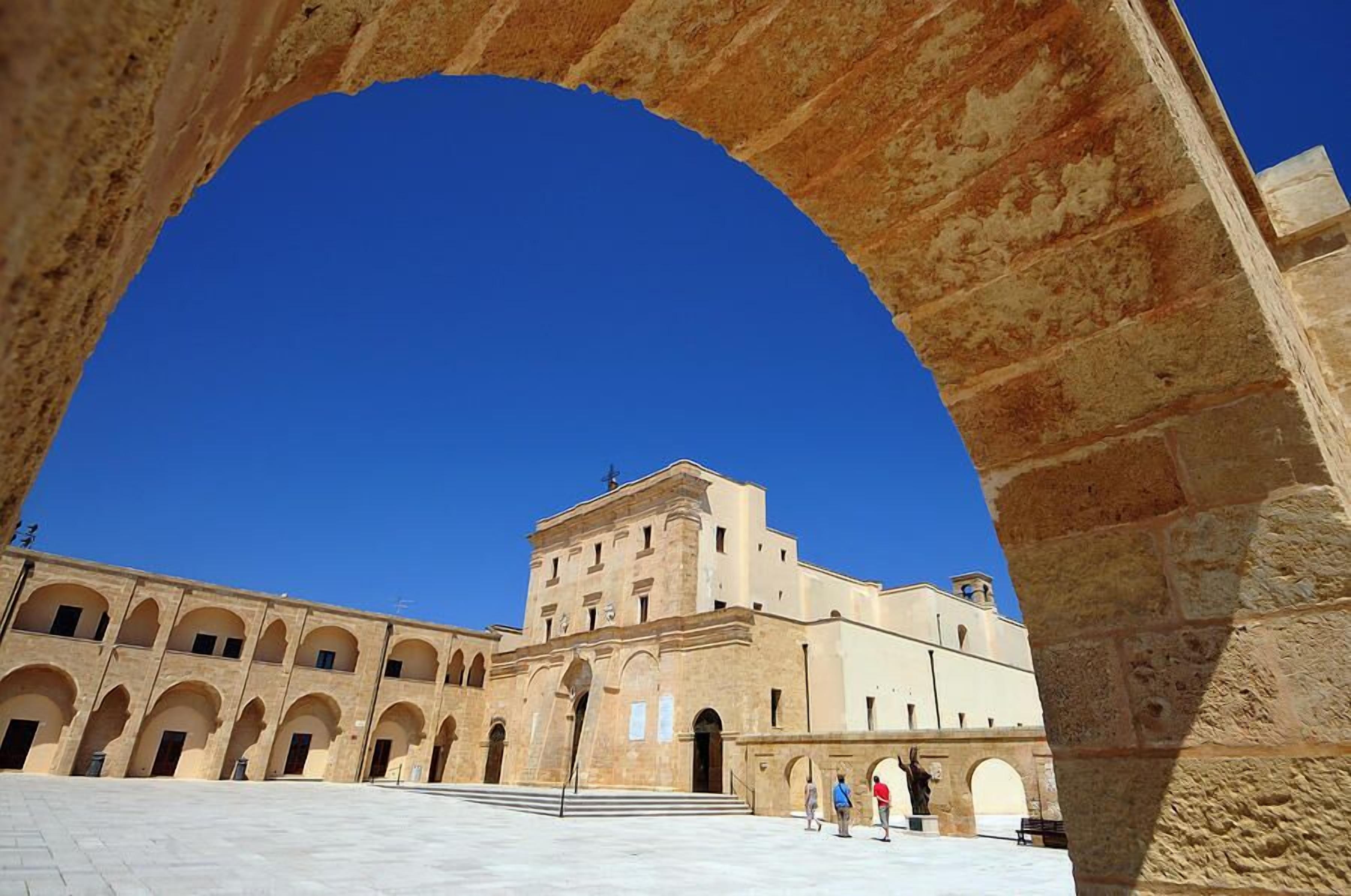 A courtyard with a large archway, a building with multiple arches, and a clear blue sky.