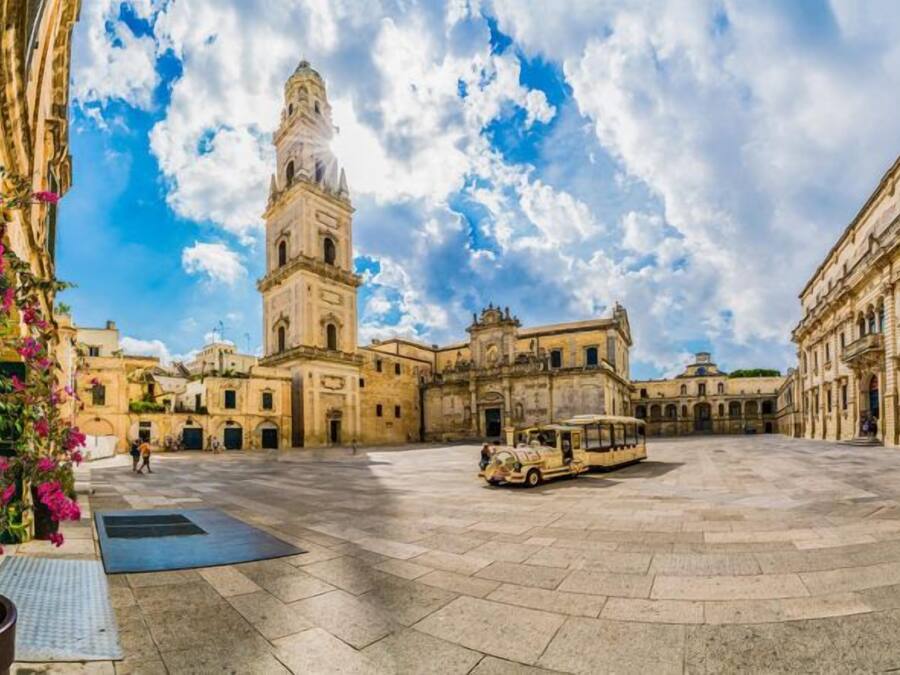 Un amplio patio con una imponente torre del reloj, rodeado de edificios históricos.