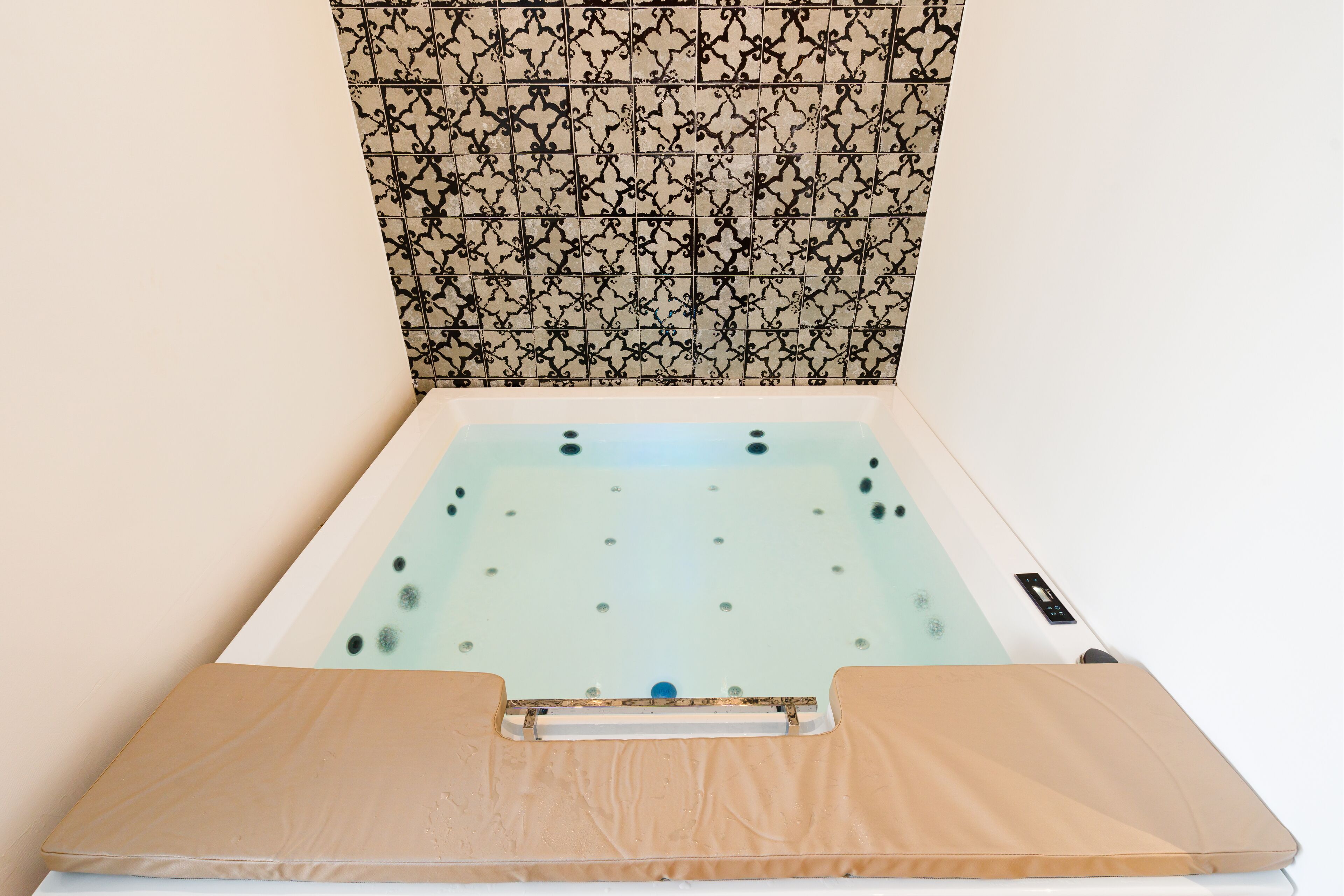 Una bañera con tapa de madera, pared con diseño y suelo de color claro.