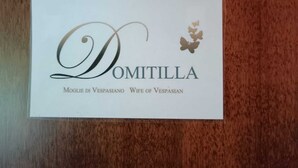 Tarjeta de presentación con el nombre "DOMITILLA" y el lema "Mogli di Vespasiano Esposa de Vespasiano".