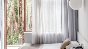 Een moderne hotelkamer met twee bedden, een groot raam met dunne gordijnen en uitzicht op palmbomen.