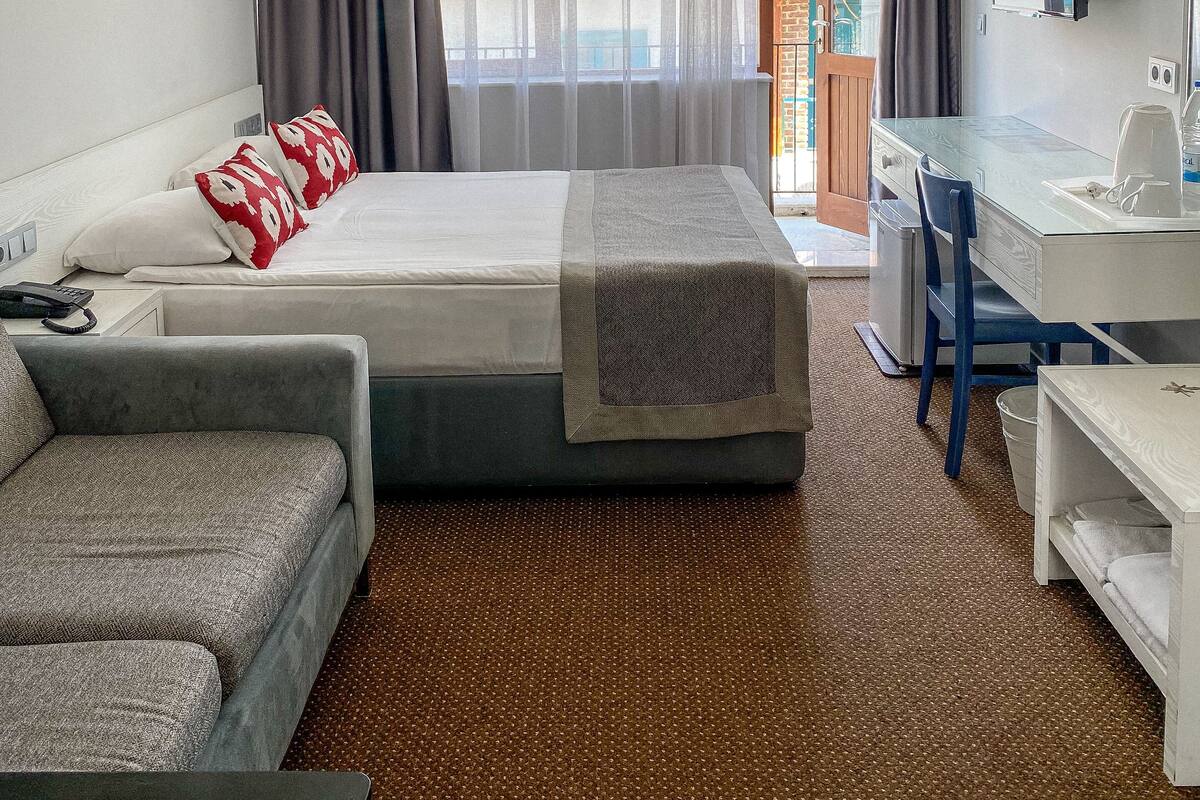 Ein Hotelzimmer mit Bett, Schreibtisch, Stuhl, Sofa und einem großen Fenster mit Vorhängen.