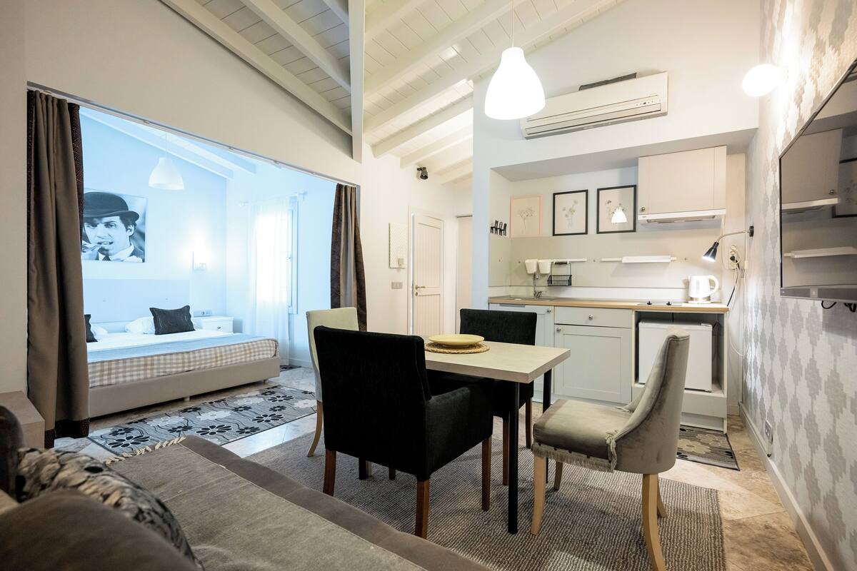 Ein modernes Hotelzimmer mit einem großen Bett, einem Essbereich mit Tisch und Stühlen, einer Küchenzeile und einem Wohnbereich mit einer Couch und einem Fernseher.