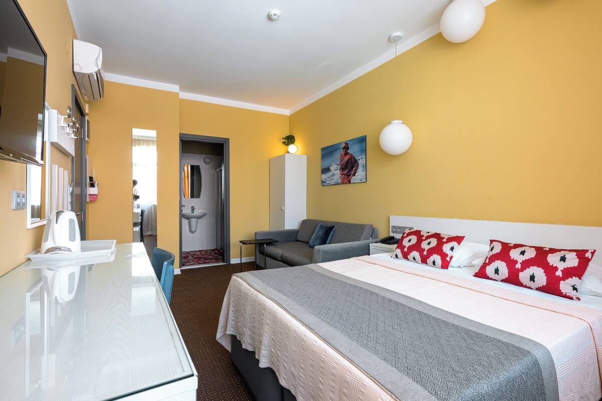 Ein Hotelzimmer mit einem Bett, einem Sofa, einem Schreibtisch, einem Spiegel und einem durchgegangenen Tür sichtbar werdenden Badezimmer.
