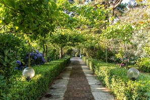 A garden pathway with a brick surface, surrounded by lush greenery and flowering plants. - Villa Hermes (San Ferdinando)