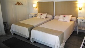 A hotel room with two single beds, each with a bedside table and lamp, a wooden ceiling, and a coat rack with hangers. - Villa Hermes (San Ferdinando)