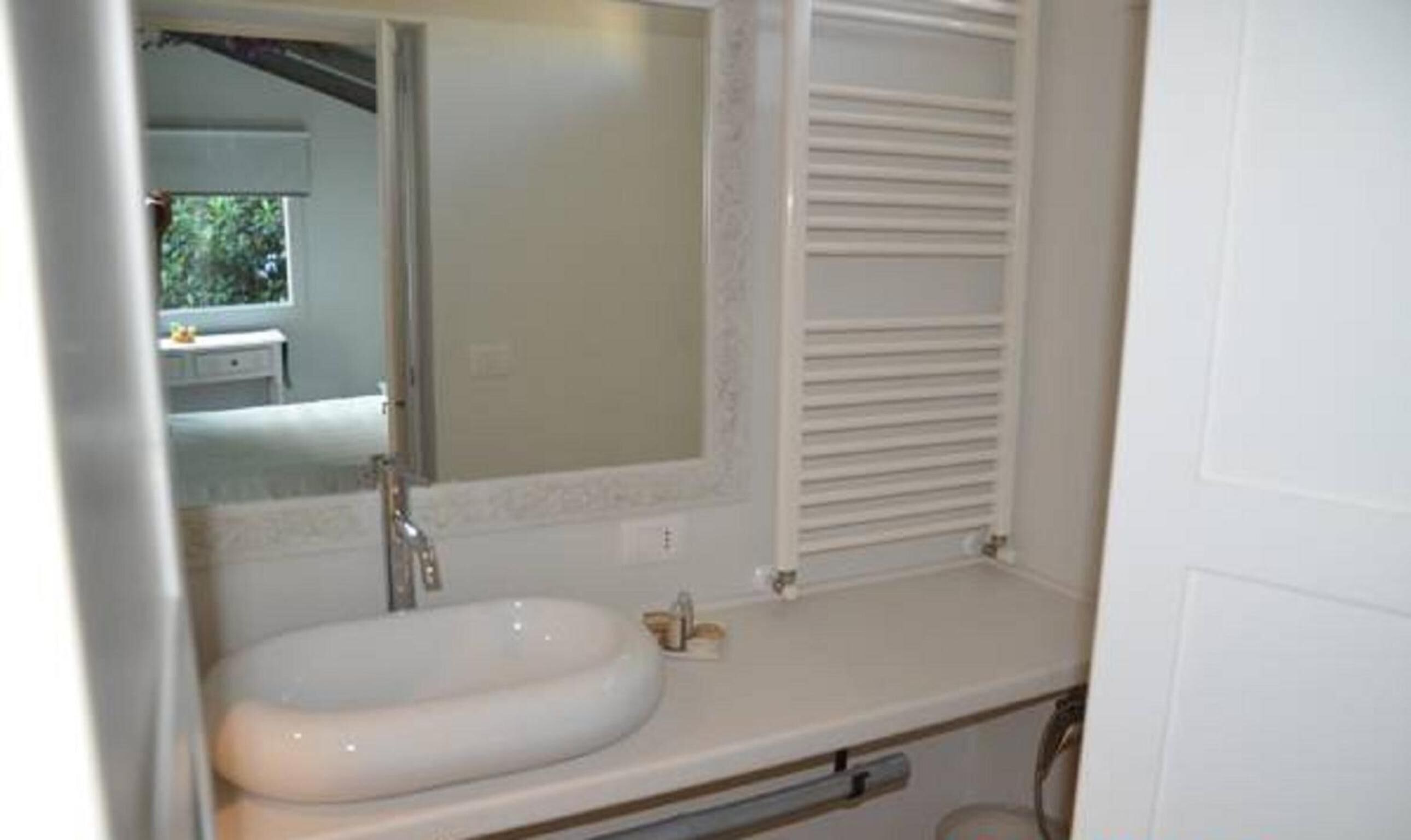 A bathroom with a white sink, a mirror, and a window with blinds.