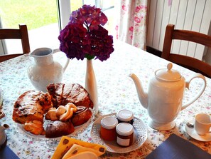 A table set with a floral tablecloth, a white teapot, a plate of pastries, a vase with purple flowers, and a pitcher. - Villa Hermes (San Ferdinando)