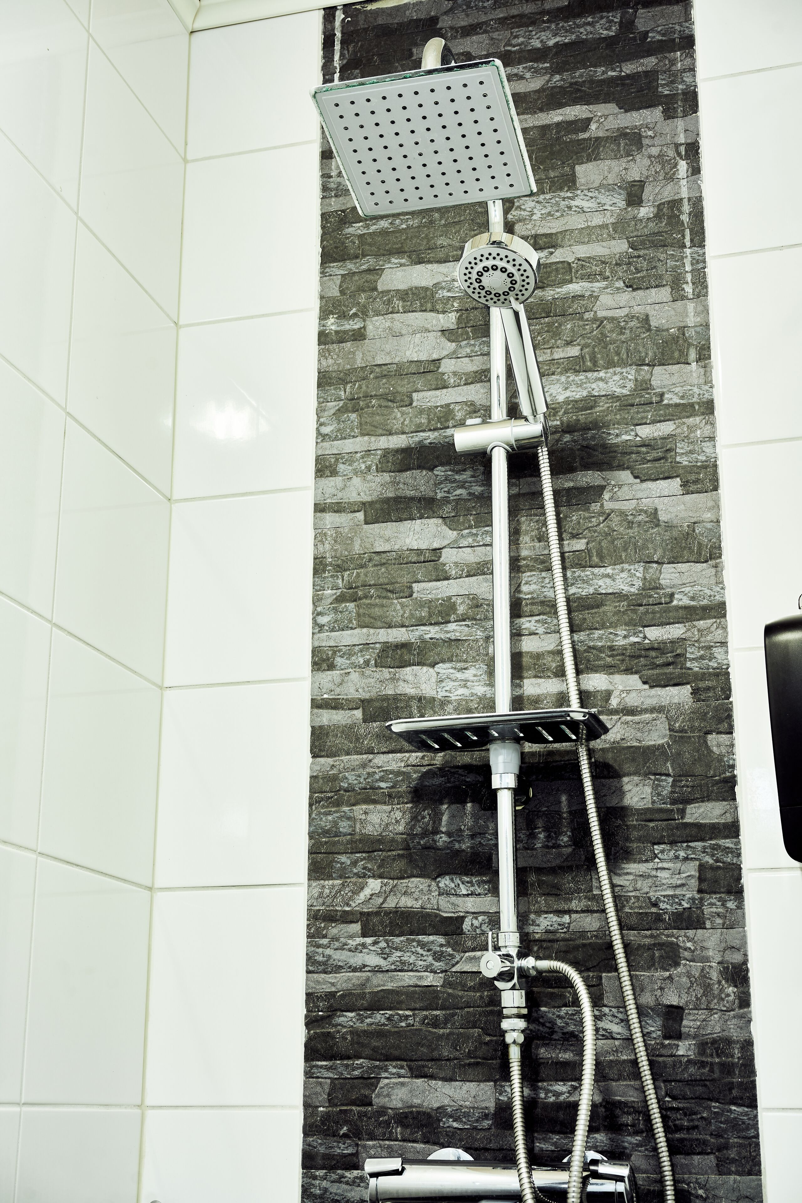 A shower with a rain showerhead and handheld showerhead, mounted on a stone wall.