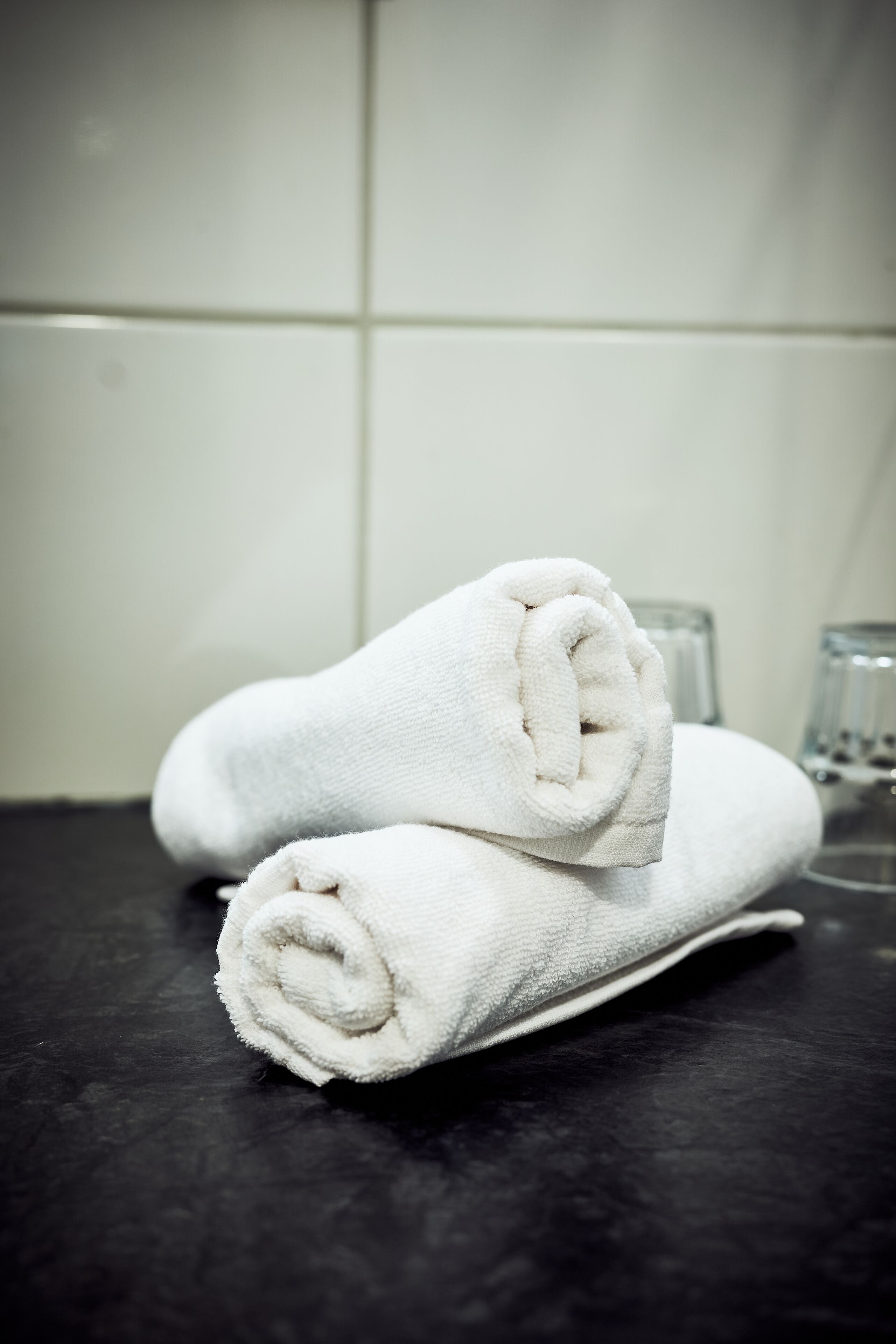 Dos toallas blancas dobladas y apiladas sobre una superficie oscura, probablemente en un baño.
