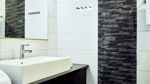 A modern bathroom with a white sink, black countertop, and a stone wall backsplash. - Hotelli Havu (Uusikaupunki)
