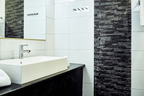 A modern bathroom with a white sink, black countertop, and a stone wall backsplash.