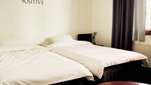 A hotel room with two beds, a nightstand with a vase, a window with curtains, and a radiator. - Hotelli Havu (Uusikaupunki)