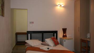 A hotel room with a bed, bedside table, lamp, and a small kitchenette area.