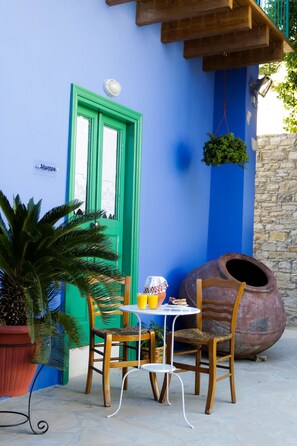 Una mesa con sillas frente a un edificio con pared azul y puerta verde.
